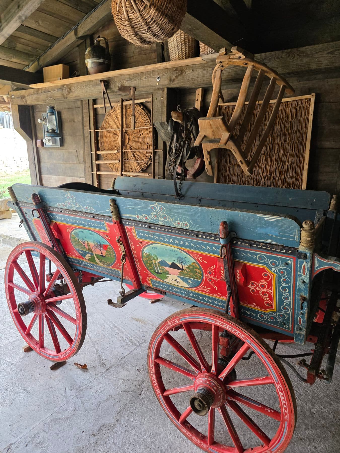A wooden cart with red wheels and painted side panels