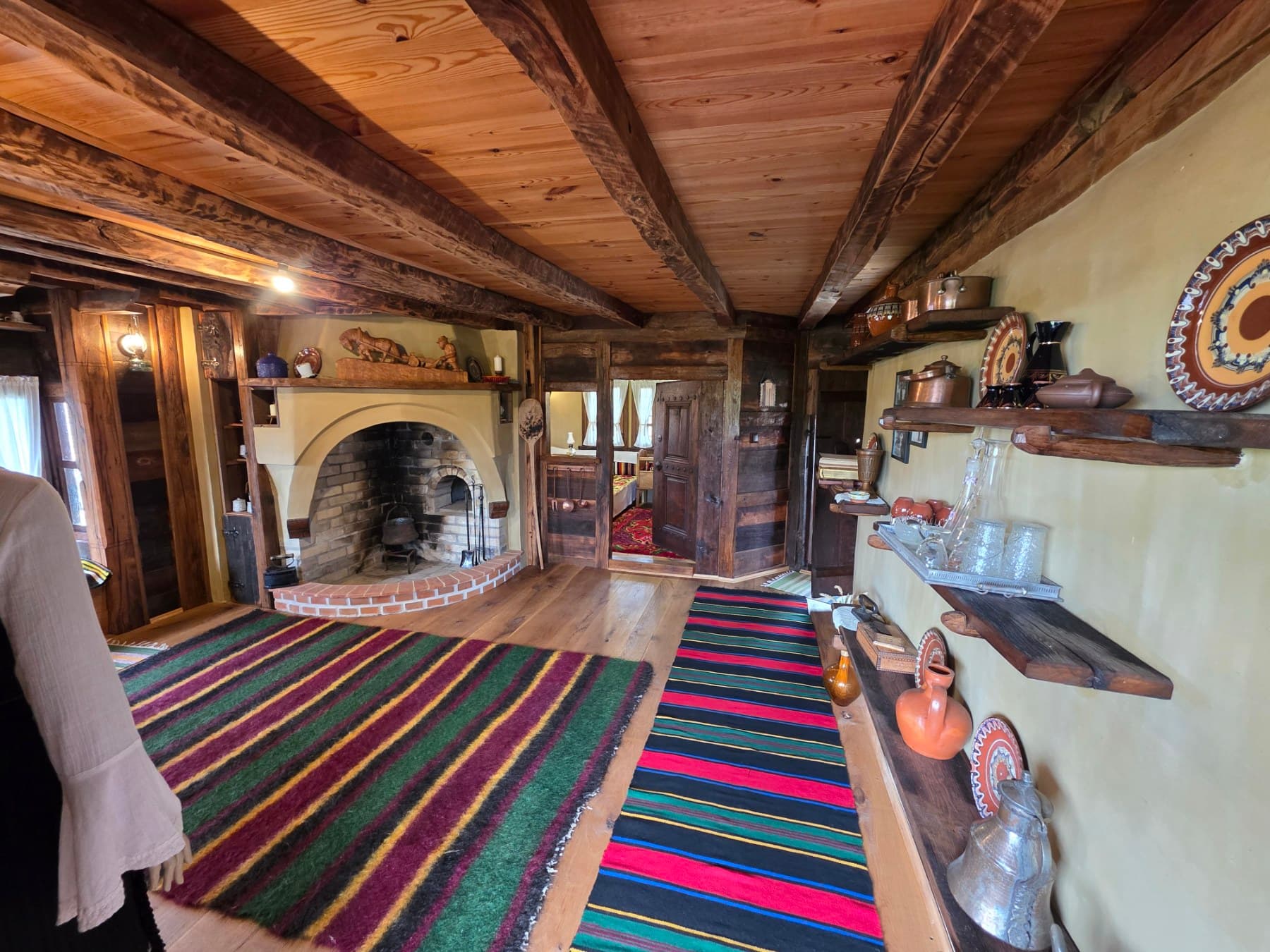 A room with a hearth, timber ceiling, colourful rugs and traditional pottery