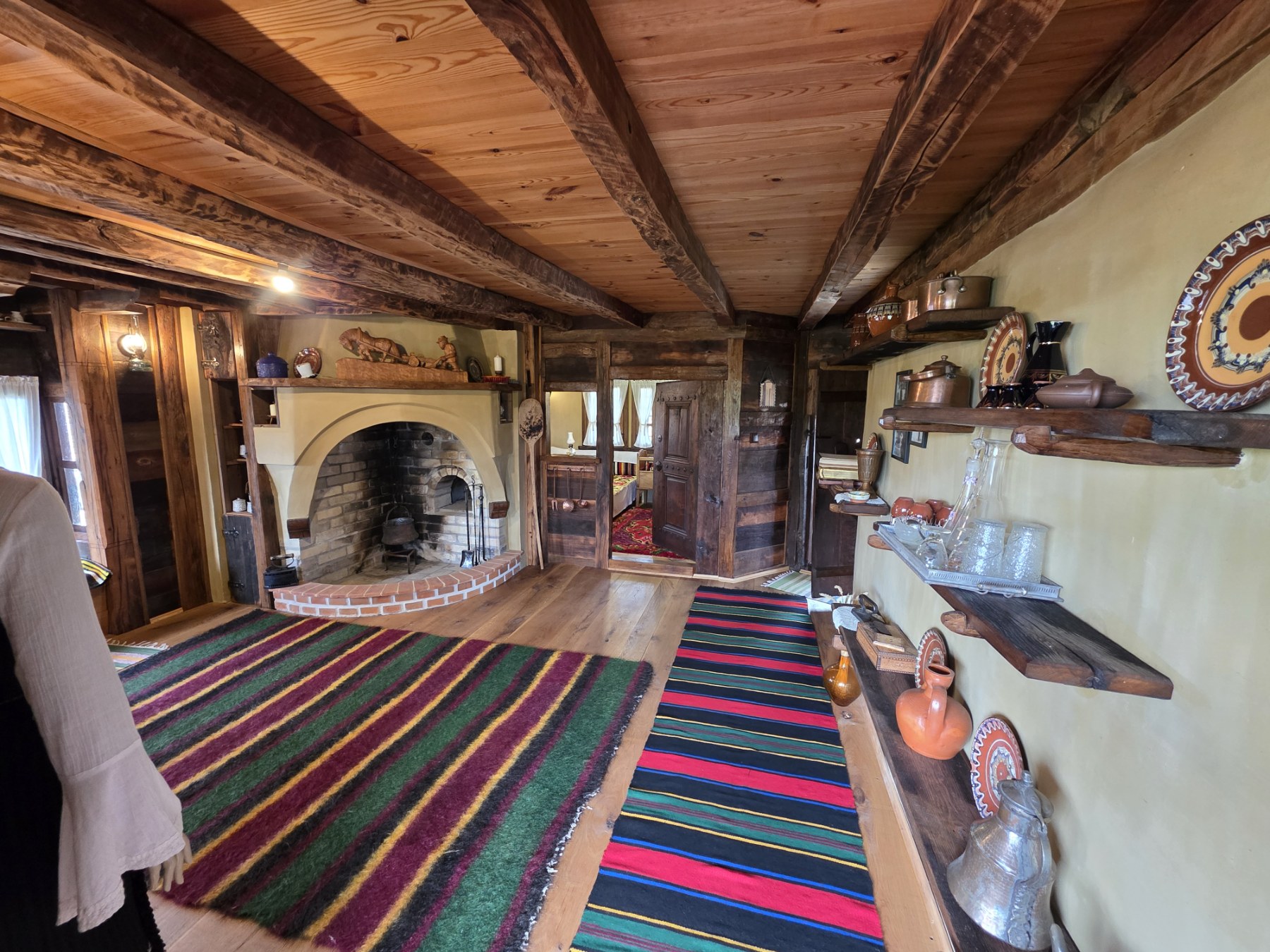 A room with a hearth, timber ceiling, colourful rugs and traditional pottery